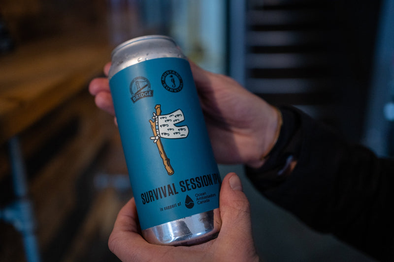 Hands hold a blue can of Survival Session IPA, a co-branded beer by Bridge Brewing and Mustang Survival.