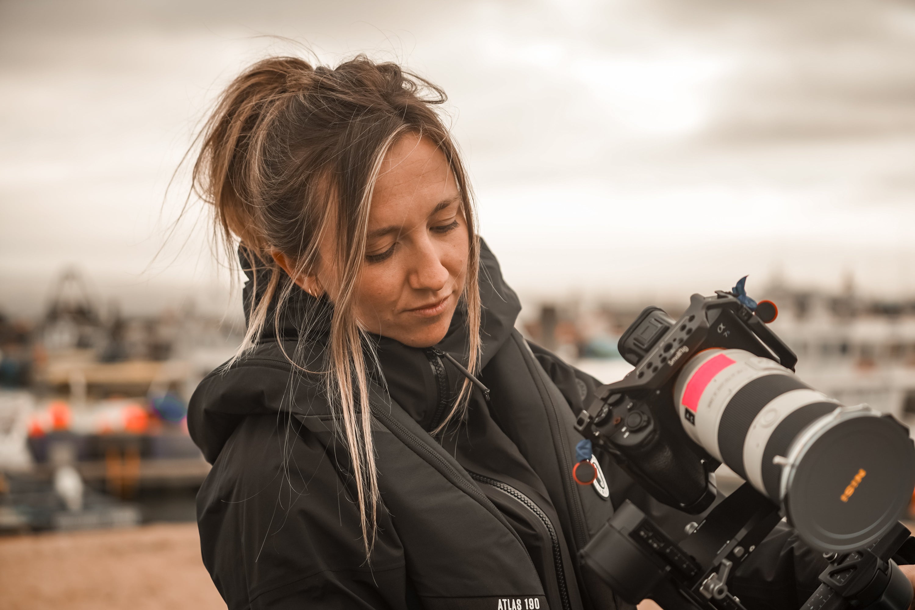Professional photographer, Alice Callow, preparing her camera gear for a shoot on the water, wearing the Atlas 190 life jacket
