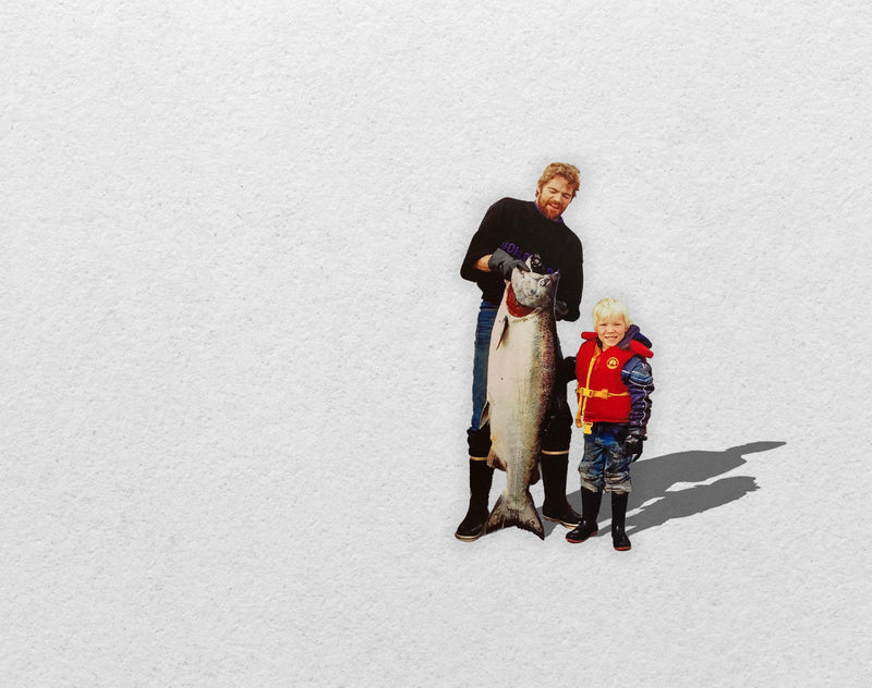 An old photo shows Don Cameron holding a large salmon next to his young son Ryan, who wears a red life jacket.