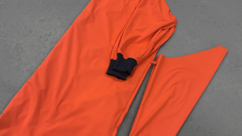 An orange medical PPE gown sample with dark fabric cuffs rests on a gray surface during pandemic prototyping.