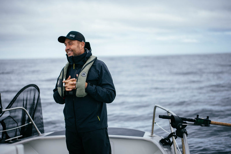 Smiling guide Yos Gladstone wears a black hat and an Elite 120 PFD while on a salmon fishing boat near Haida Gwaii.