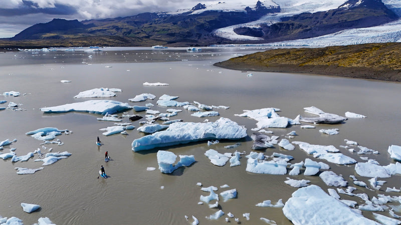An aerial view of three paddlers in Mustang Survival drysuits navigating paddleboards through icebergs in Iceland.