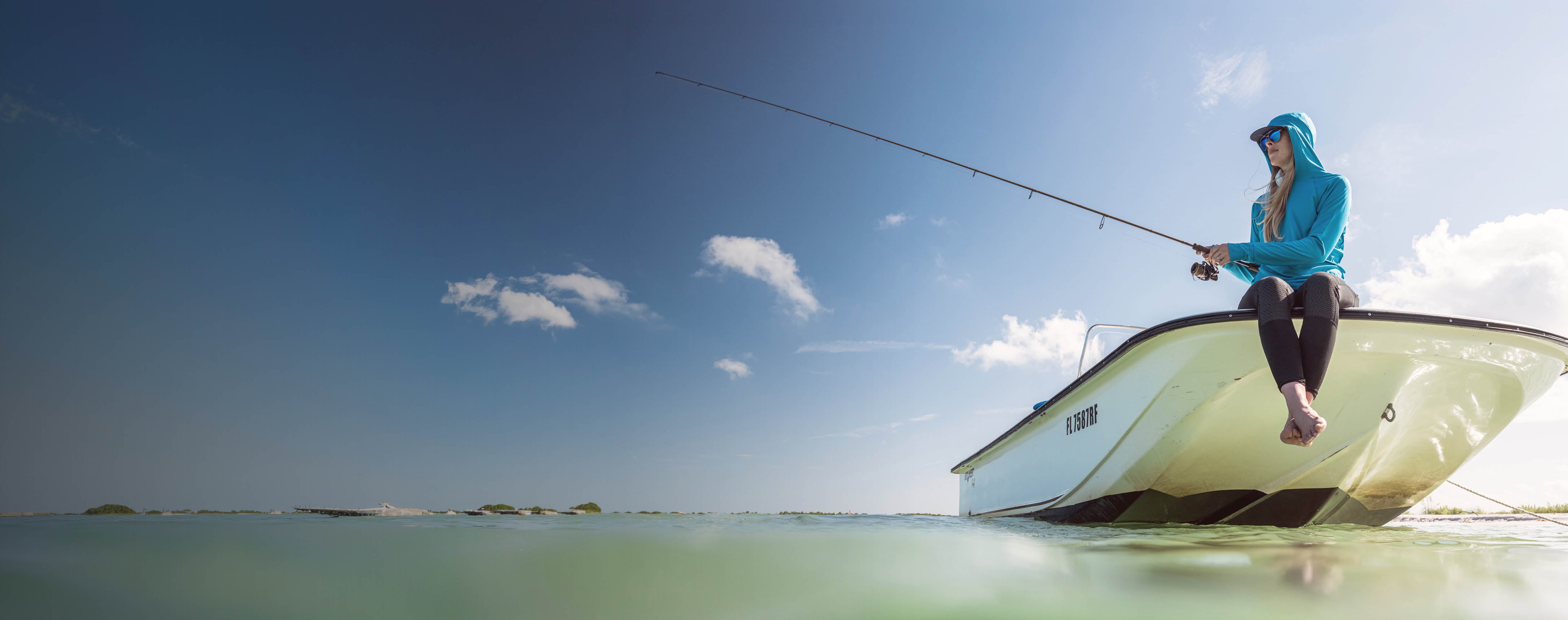 Woman fishing from a small boat on a clear day with blue sky and green water.
