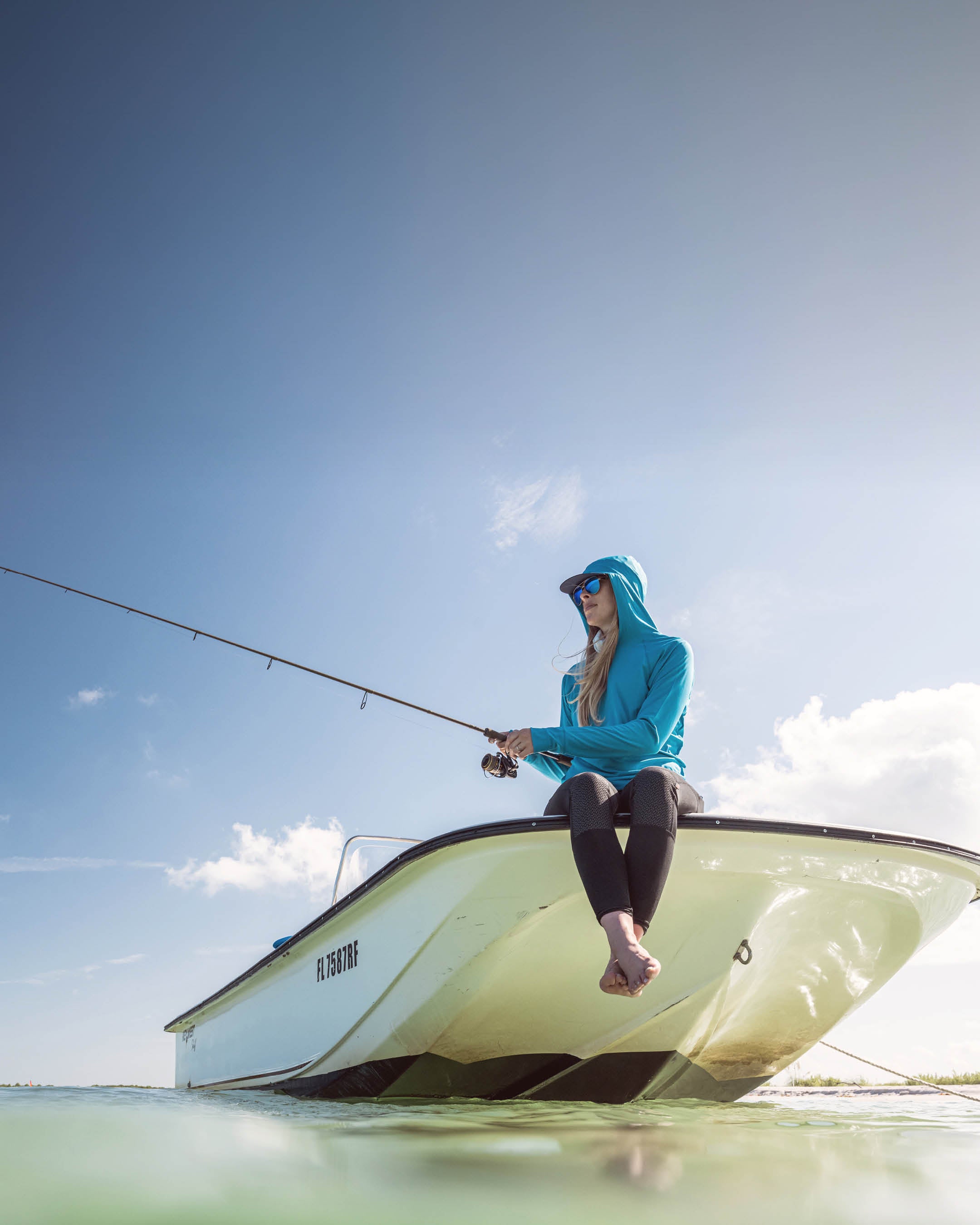 Woman fishing from a small boat on a clear day with blue sky and green water.
